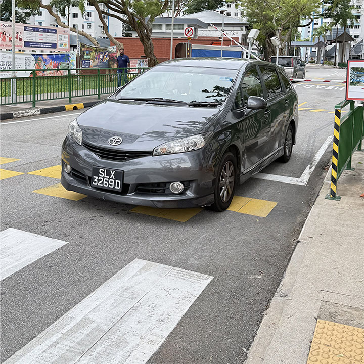 A car stopped directly on top of the zebra crossing, blocking the pedestrian path